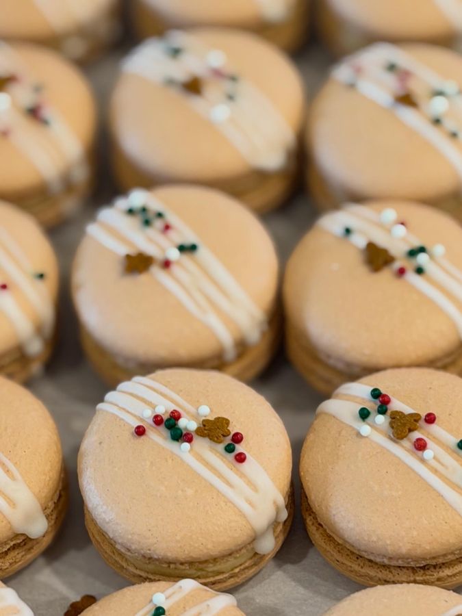 Peach gingerbread macarons drizzled with white icing and holiday sprinkles