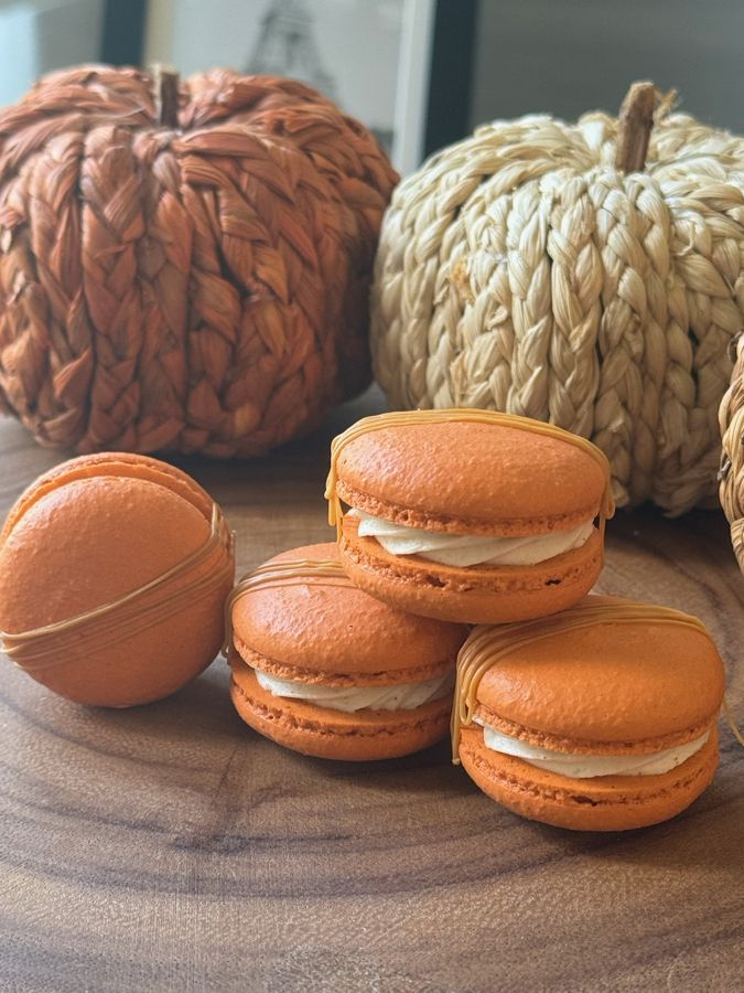 Orange pumpkin spice macarons stacked beside woven pumpkins