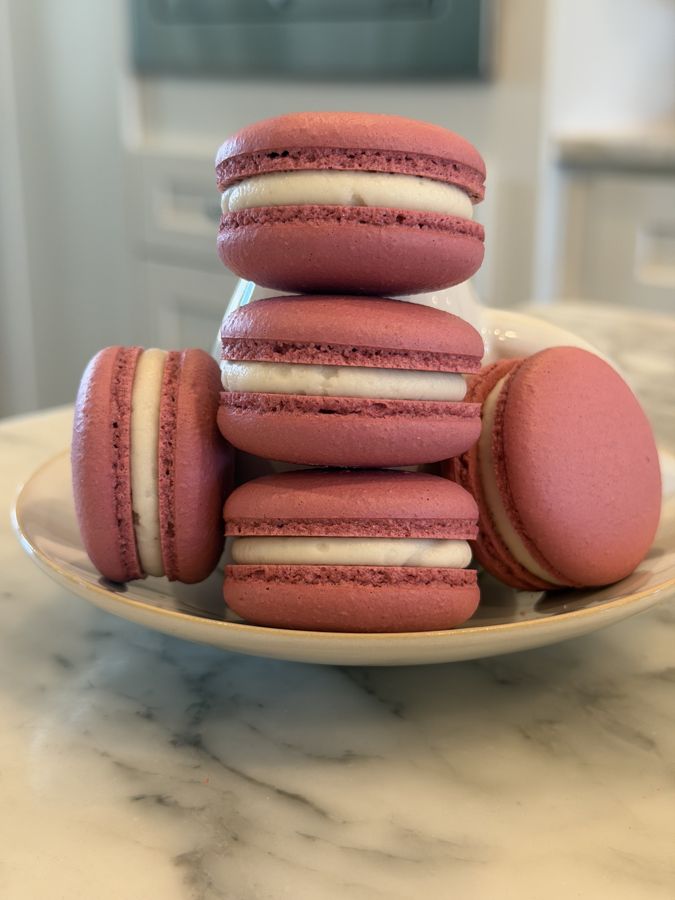Rose-pink macarons stacked on a white plate on a marble counter