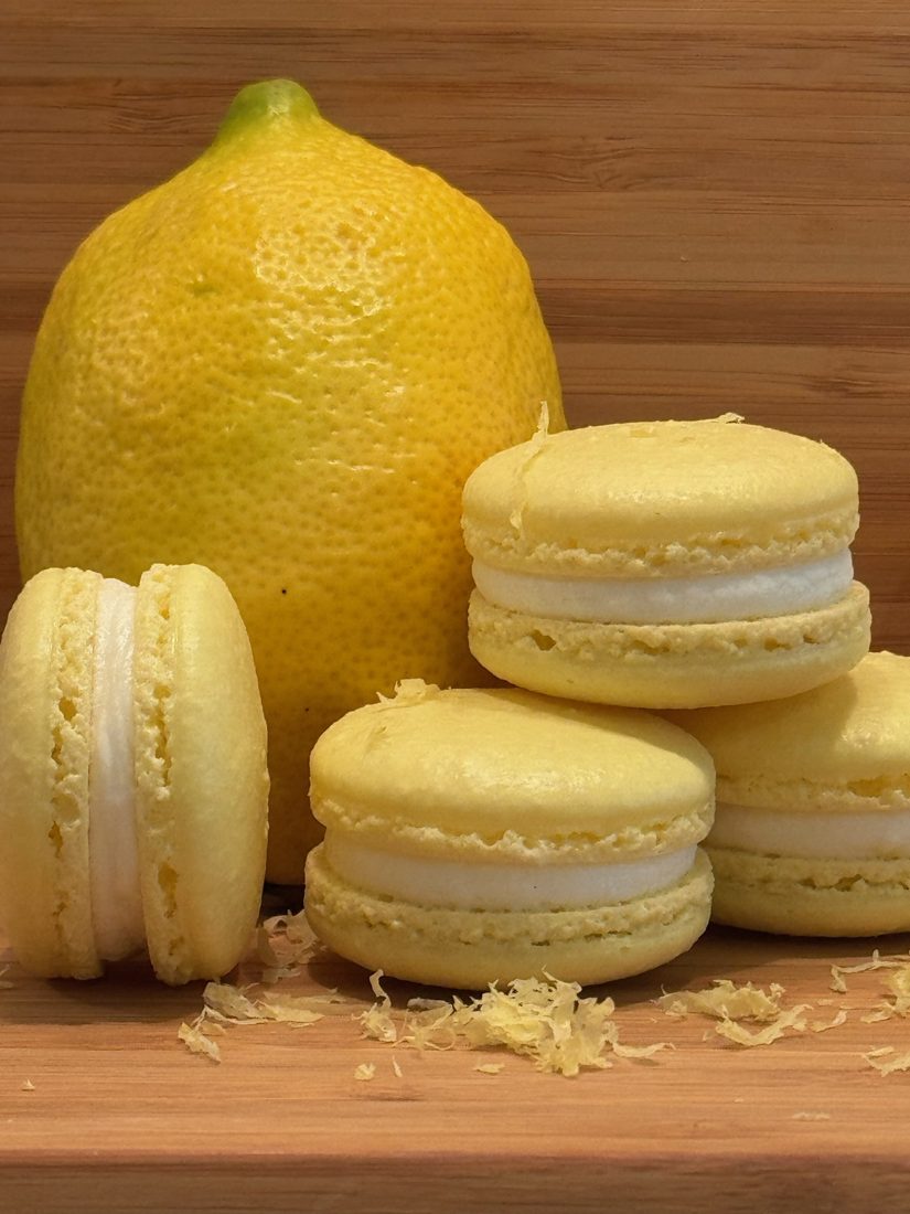 Pale yellow lemon macarons stacked beside a whole lemon and fresh zest