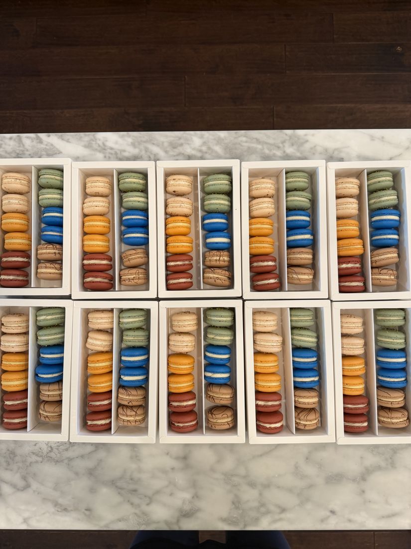Ten white window boxes of macarons in fall colors laid out on a marble counter