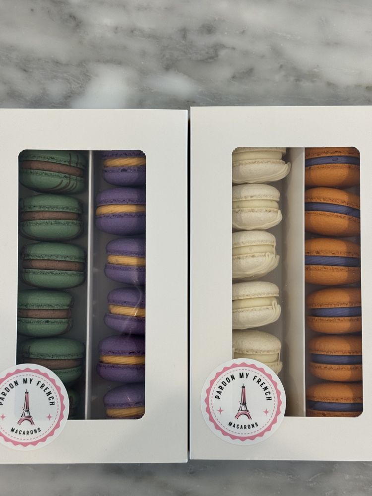 Two white window boxes of macarons in green, purple, white, and orange