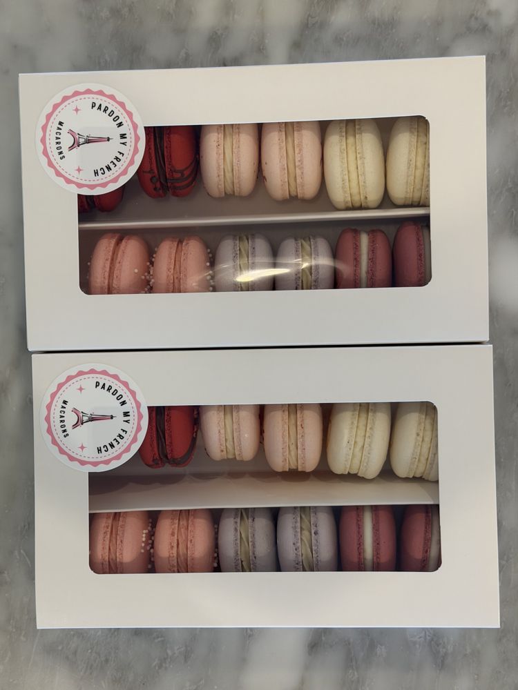 Two white window gift boxes, each with the Pardon My French seal, holding pastel macarons in two rows